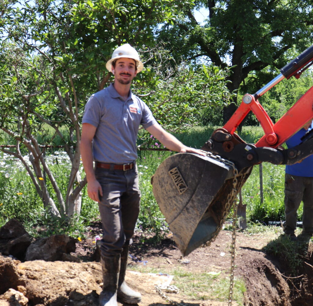 Sewer Line Crew Member next to an Excavator