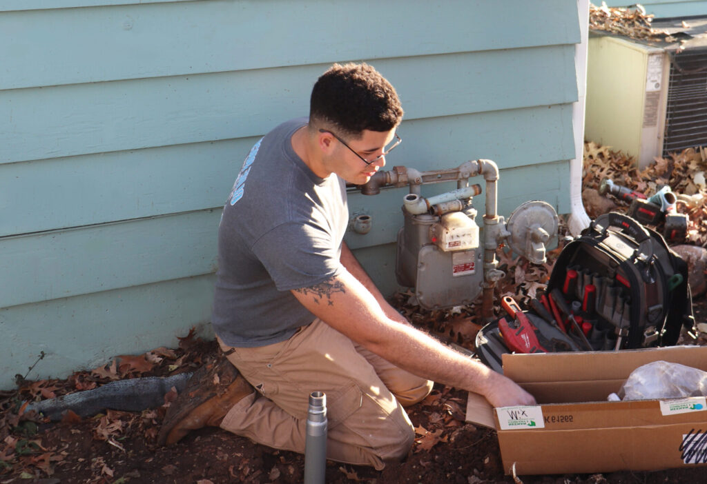 Plumber kneeling beside a home adjusting a gas meter and preparing tools for a gas line installation.